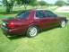 2004 Ford Crown Victoria - This maroon sedan is seen from a rear three-quarter angle, parked on a grassy area with trees in the background.