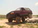 1992 Ford Bronco - A maroon 1992 Ford Bronco navigates a rocky terrain, demonstrating its off-road capabilities.
