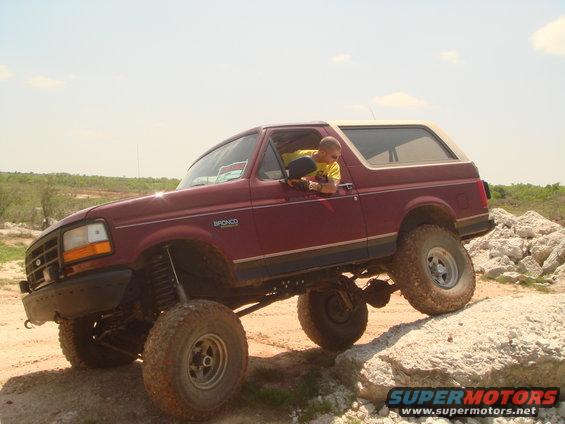 Maroon 1992 Ford Bronco with a tan top, lifted suspension, driving over rocks