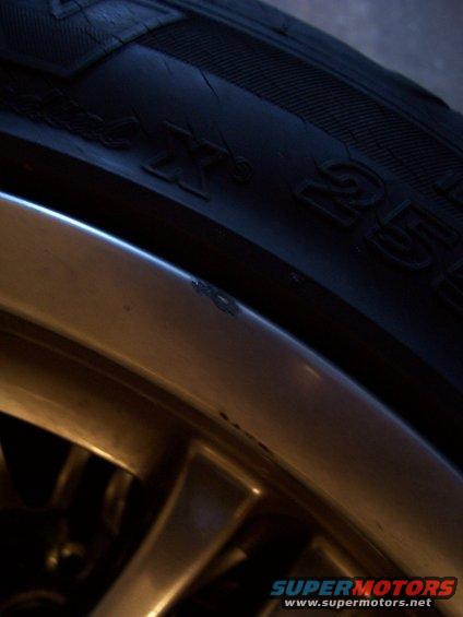 Close-up of a tire with visible text and a scratched alloy wheel