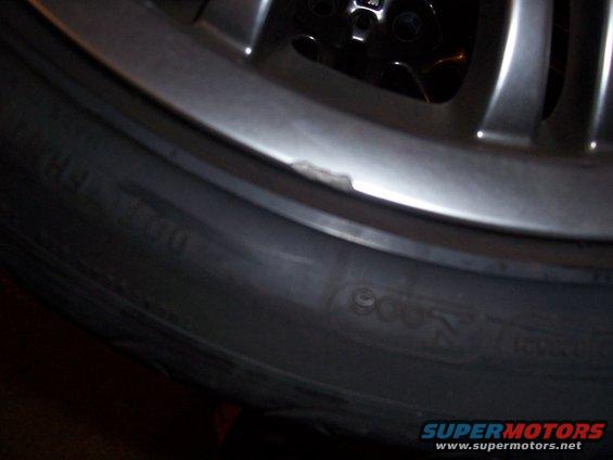 Close-up of a damaged alloy wheel and tire sidewall with visible text