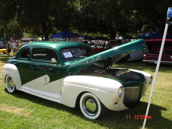 Green and white coupe with hood open, parked on grass at an outdoor event