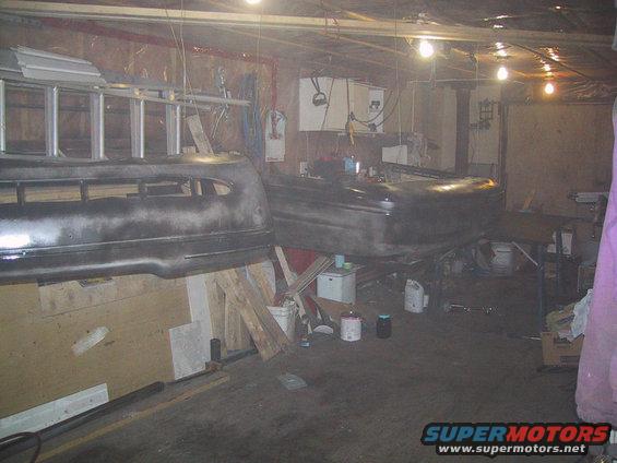 Car bumper and hood in a garage, possibly being prepped for paint