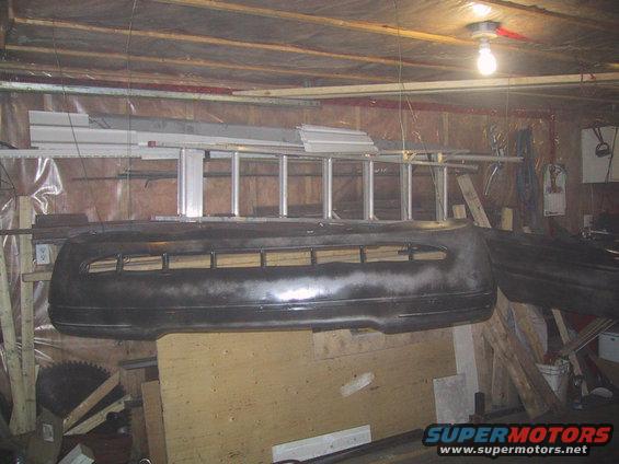 Ford Crown Victoria front bumper hanging in garage, with ladder and tools in background