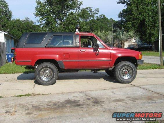 Red 1987 Toyota 4Runner with black camper shell, side view