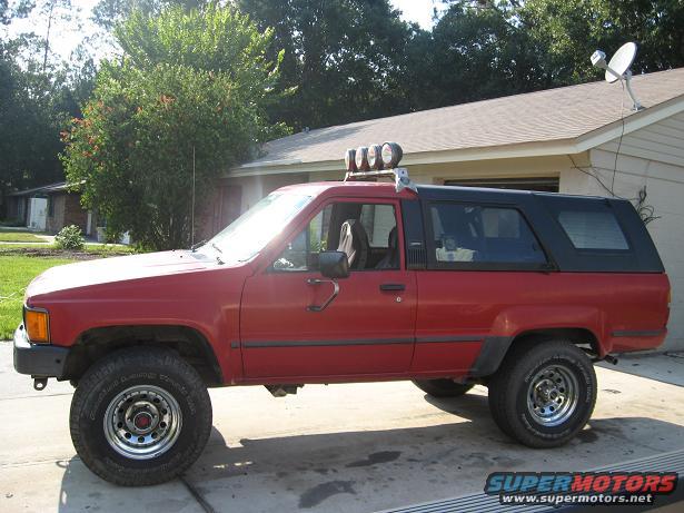 Red Toyota 4Runner, second generation, with a black camper shell and roof lights, parked on a driveway