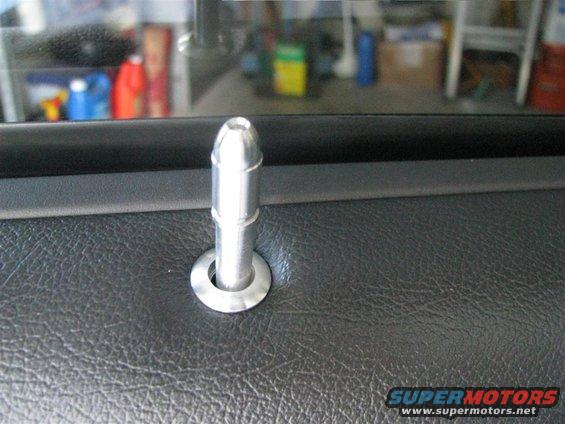 Close-up of a silver door lock pin on a black interior door panel. Text at bottom reads SUPERMOTORS
