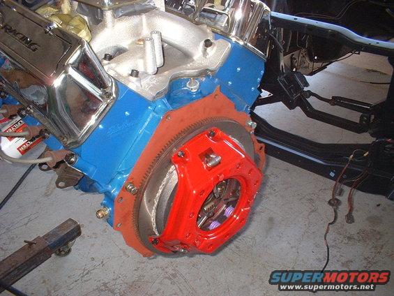 Blue engine block with chrome valve covers and red clutch housing. Part of a vehicle frame is visible