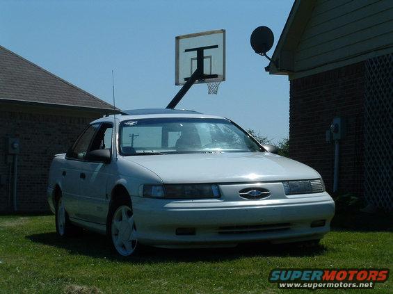 Front view of a white 1992 Ford Taurus sedan parked on grass, with a basketball hoop and house in the background