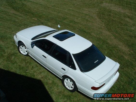 White sedan parked on grass, seen from above. Has a sunroof