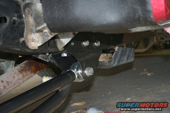 Close-up of an aftermarket suspension component bolted to a vehicle's frame, with part of the exhaust visible