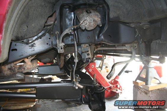 Underside view of a vehicle's front suspension with parts removed, supported by jack stands