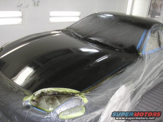 Black car hood and windshield covered in plastic sheeting, taped for painting