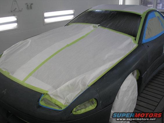 Car hood and front fender taped off for painting. A Mitsubishi logo is visible on the fender