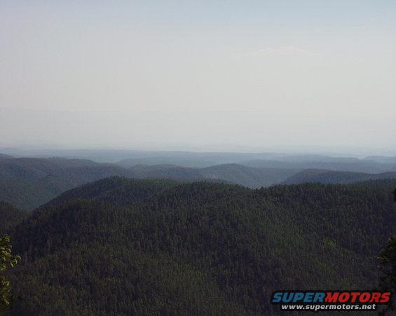 Hazy mountain range with evergreen trees under a pale sky. Text 'SUPERMOTORS' visible
