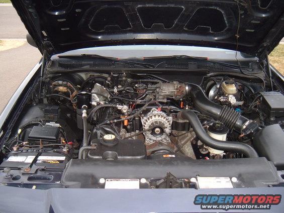 Engine bay with alternator, air intake, and battery visible. Supermotors.net logo at bottom