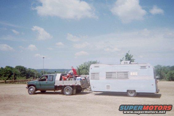 Green flatbed truck towing a white camper trailer, side view