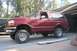 1989 Ford Bronco - This lifted red Ford Bronco SUV has a side profile view, showing its chrome trim and aftermarket wheels.