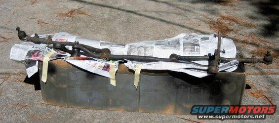 Steering linkage components laid out on newspaper and a dark container