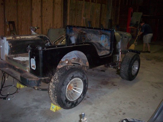 Black Jeep CJ-series body on jack stands, missing doors and windshield, in a workshop