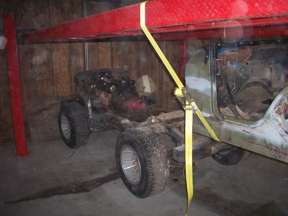 Jeep CJ-series chassis suspended by yellow straps under a red lift