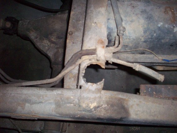 rusted frame with fuel lines and brake lines, showing a hole in the frame