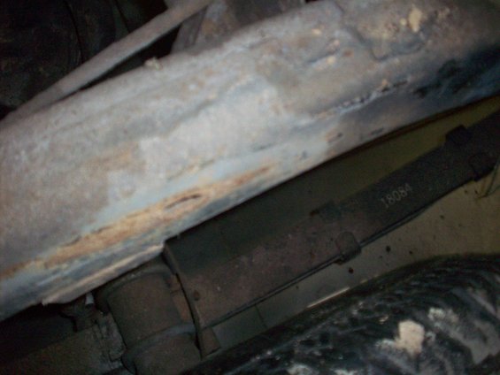 Close-up of a leaf spring with '18084' stamped on it, part of a vehicle's undercarriage