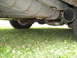 1984 Mercury Grand Marquis - The exhaust system and fuel tank are visible from underneath the vehicle, with grass below.