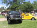 2001 Chevrolet Silverado 1500 - A black pickup truck and a yellow hot rod are displayed on a grassy field with people in the background.