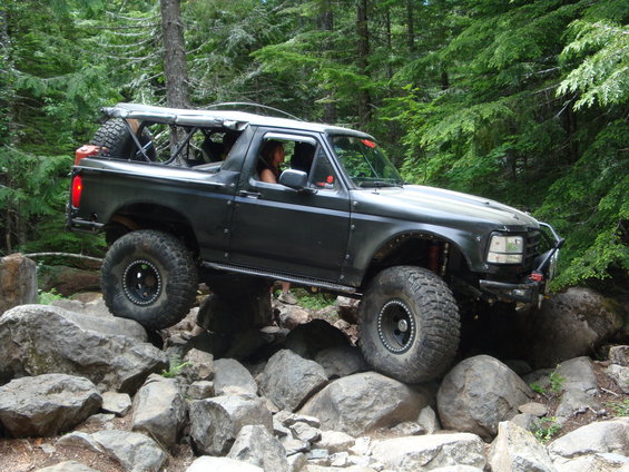 Modified dark gray Ford Bronco with large tires navigating a rocky trail