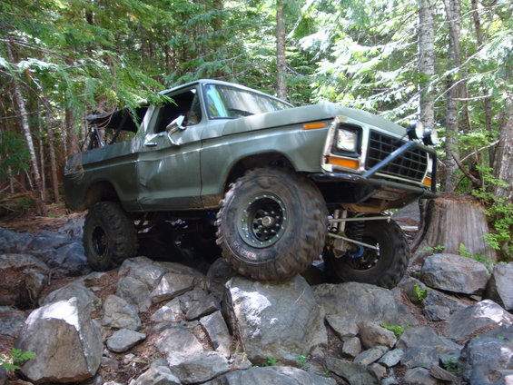 Modified 1978 Ford Bronco climbing over large rocks on a wooded trail