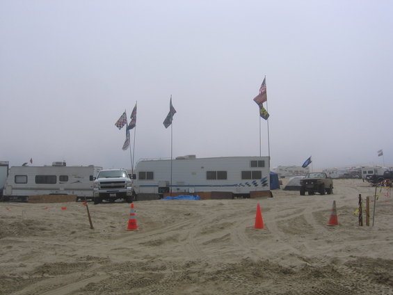 White pickup truck parked on a sandy beach with RVs and flags