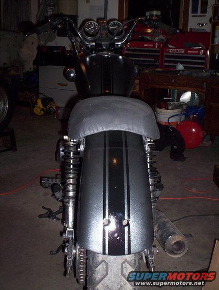 Motorcycle rear fender with black and silver stripes, and a black seat. Exhaust pipe visible on the right
