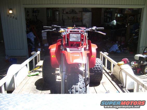 Red three-wheeled ATV on a trailer, front view. Tires are knobby, handlebars are visible