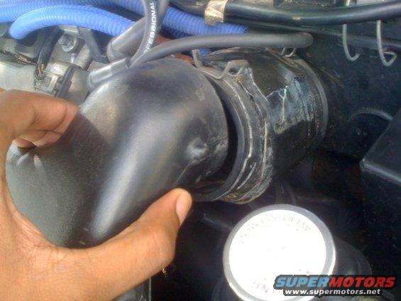 Hand holding black rubber engine intake hose near cracked connector