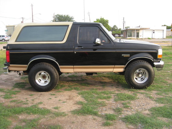 Black and tan Ford Bronco parked on dirt and grass. Side view