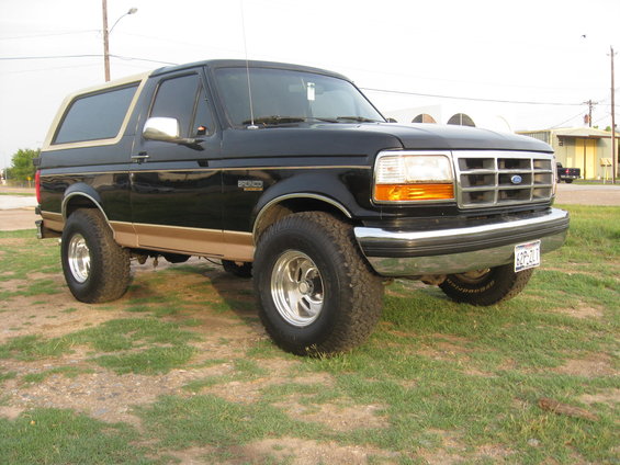 Black Ford Bronco with tan trim, lifted suspension, and chrome wheels parked on grass