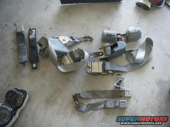 Disassembled gray seat belts and a dashboard gauge cluster on a concrete floor