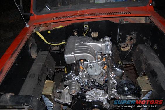 Engine bay showing a V8 engine with a silver intake manifold and orange fuel injectors. The vehicle is red