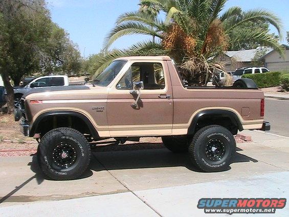 Lifted brown and tan Ford Bronco parked on driveway, palm tree behind it. Other vehicles visible in background