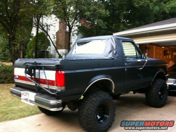 Black Ford Bronco with a soft top, lifted suspension, and off-road tires, viewed from the rear three-quarter angle