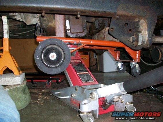 Vehicle undercarriage supported by jack stands and a floor jack. Orange support arm visible