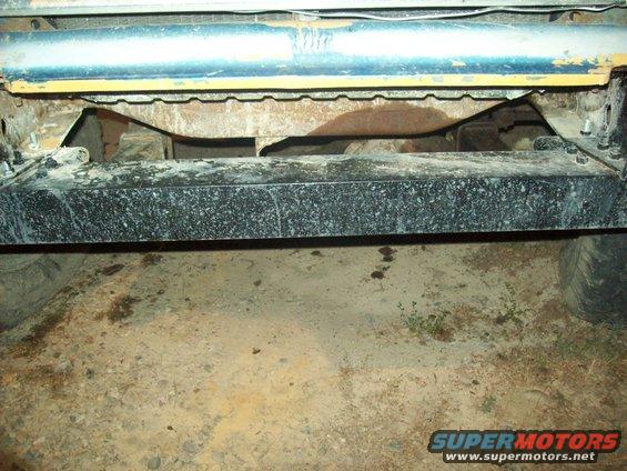 Underside of a truck, showing the frame, bumper, and suspension components. Tires are visible on the sides