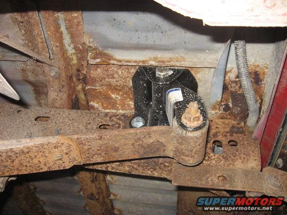 Underbody view of rusty frame with black bracket and bolts