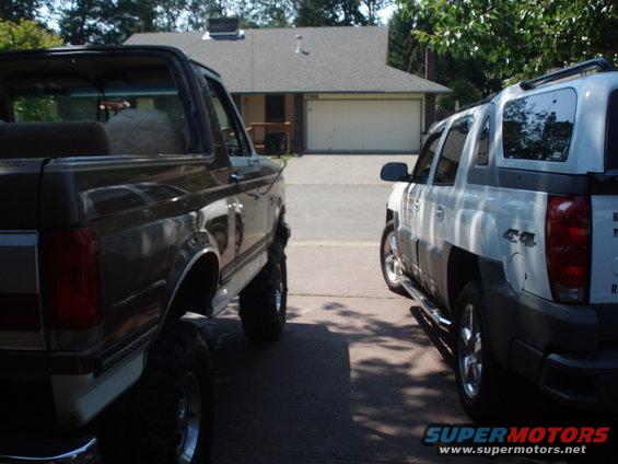 Dark brown Ford Bronco with lifted suspension and chrome wheels parked next to a white Chevrolet Avalanche