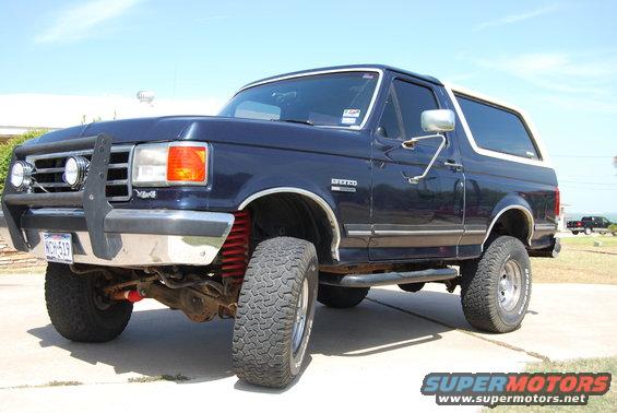 Dark blue Ford Bronco with a white top, lifted with off-road tires. Has a brush guard on the front bumper