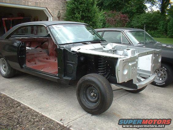 Black 1967 Mercury Cyclone body, stripped down, parked on a driveway next to another car