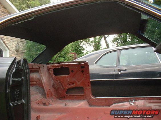 1967 Mercury Cyclone interior under restoration, showing bare metal and headliner. Black car visible through open door