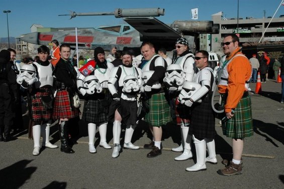 Group of people dressed as stormtroopers with some wearing kilts, standing in front of a prop spaceship