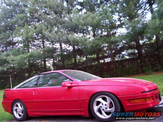 Red coupe parked outside with trees in the background
